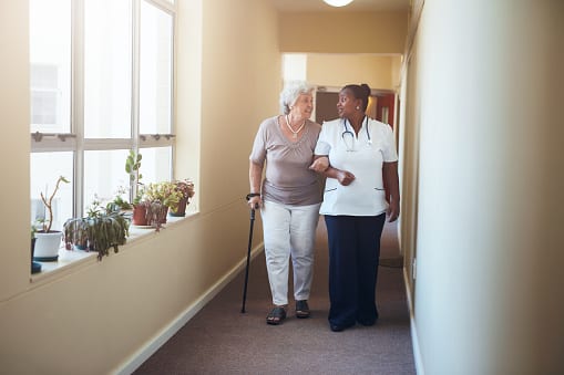 A resident is engaged in conversation as she gets assistance with walking from place to place.