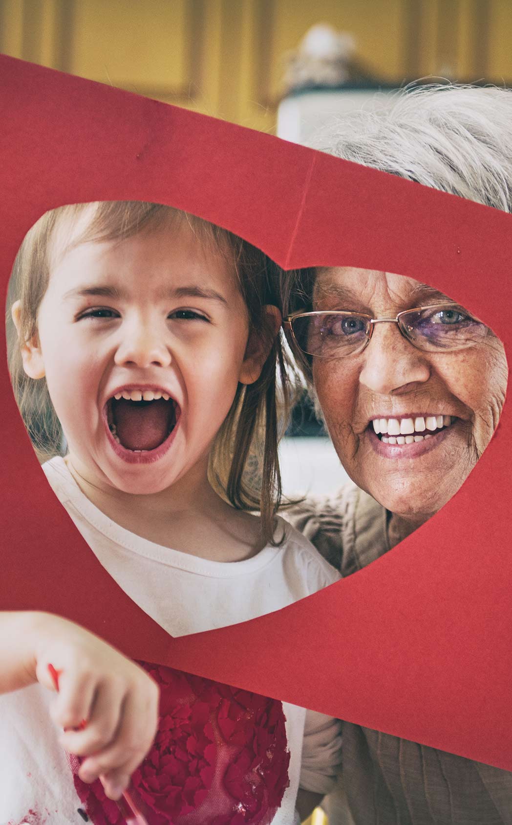 A grandmother and granddaughter pose for the camera through a paper heart.