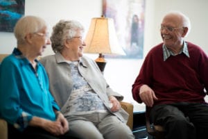 A man and two women have a pleasant conversation in a social area of the assisted living facility.