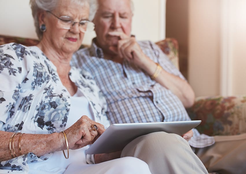 A senior couple deliberate while operating an iPad tablet as they sit on their private apartment couch.