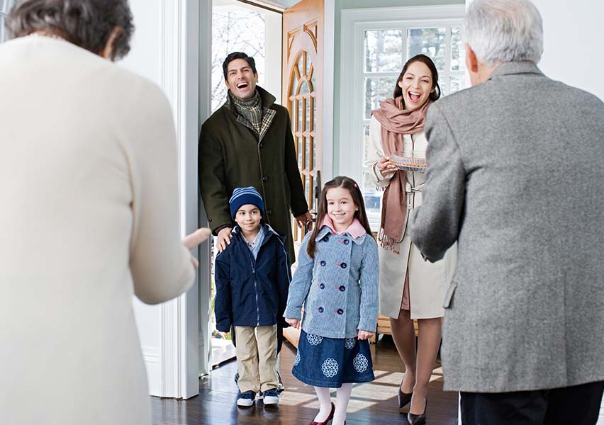 A grown framily with two kids excitedly enter the front doors to visit with parents/grandparents.