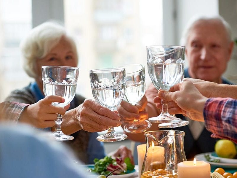 Senior residents celebrate being hydrated by all clicking their drinking glasses together across a shared dining table.