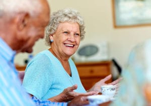An amused female resident with her palms raised sits down for tea among others.