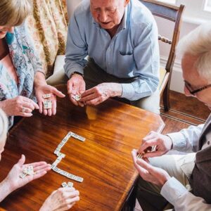 Four assisted living residents are playing dominos together in a recreation room where board games are available.
