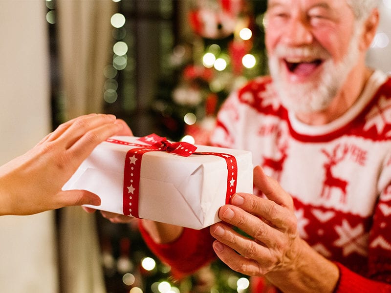 An excited male resident receives a christmas gift in a box with a bow.