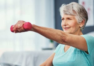A fit elderly woman holds an exercise pose meant to build strength while extending her arm in front of her with a free weight.