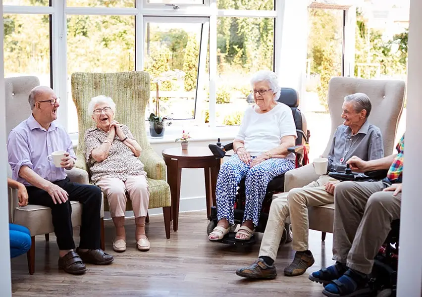 Six people sit in the facility sun room socializing over drinks.