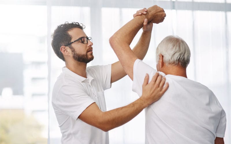 A physical therapist helps an older man with a stretch.