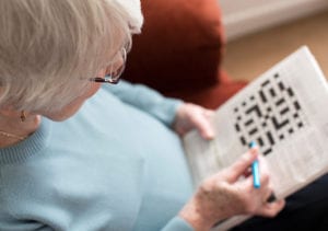 A senior resident does a crossword puzzle while she sits on an armchair in her private apartment.