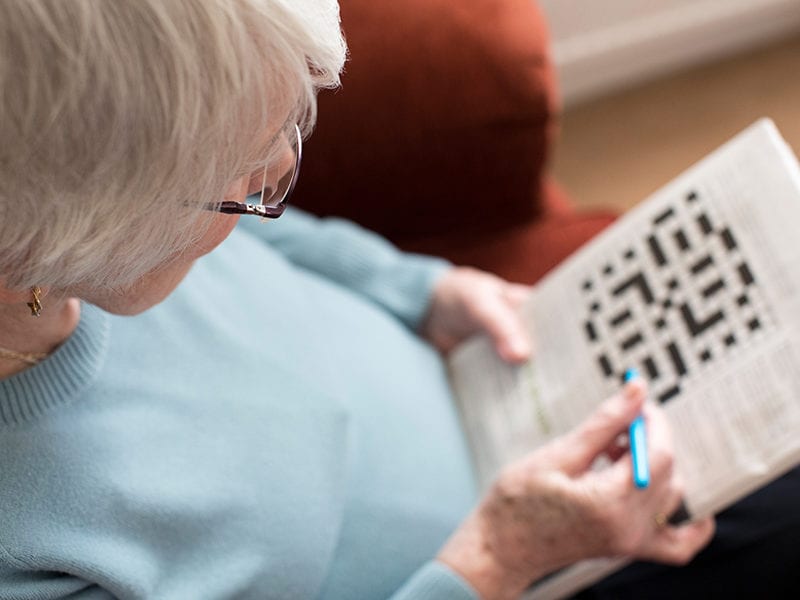 A senior resident does a crossword puzzle while she sits on an armchair in her private apartment.