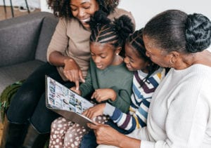 Four family members read from a scrapbook of memories and views pictures together while sitting on an apartment couch.