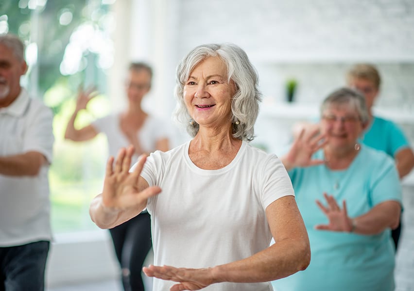 A senior Culpepper Place woman resident is doing low impact movements among friends in an exercise class.