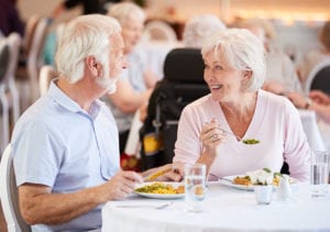 Two senior residents eat in the dining room cafeteria and have an engaging conversation over their meals.