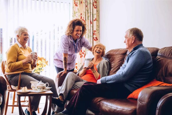 A female Culpepper Place staff member shares a laugh with a senior couple and their friend while discussing the security of the facility