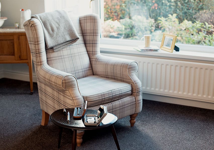 A gray armchair sits by a window in an assisted living facility