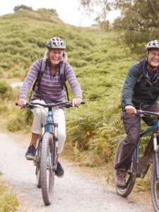 Two senior citizens enjoying spring activities by riding their bikes on a trail near their assisted living facility.